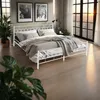 A bedroom scene with a white metal bed frame, bedding, plants, and a large window with sunset views. Náhled obrázku produktu