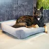 A German Shepherd dog is resting on a dog bed in a modern interior setting. Produktbild-Vorschau