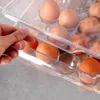 A hand is shown adjusting a clear plastic egg container filled with brown eggs. Náhled obrázku produktu