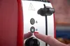 A close-up shot of a red toaster with a person's finger pressing a button. Náhľad obrázku produktu