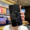 A person is holding a black phone case with a magnetic ring on the back, in what appears to be a cafe or store. Náhled obrázku produktu