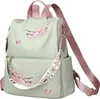 A light green backpack with pink accents and floral embroidery, displayed against a white background. Náhľad obrázku produktu