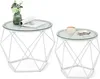 Two white geometric side tables with glass tops, one with a vase of flowers and a magazine, the other with a cup and macarons. Náhled obrázku produktu