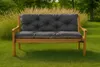 A dark gray tufted cushion sits on a wooden garden bench in a grassy yard with tall dry grass behind it. Produktbild-Vorschau
