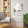 A modern living room setting with a grey armchair, a white dresser, and a round golden mirror on the wall. Produktbild-Vorschau