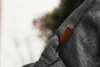 A close-up of a dark gray fabric with a small brown leather tag attached. Produktbild-Vorschau