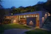 A modern house built into a hillside at dusk, with exterior lighting. Anteprima dell’immagine prodotto
