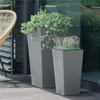 Two tall grey planters with plants on a wooden deck next to a glass door. Voir les images du produit