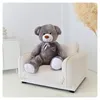 A large gray teddy bear is sitting on a small, cream-colored armchair in a brightly lit room. Podgląd zdjęcia produktu