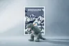 A plush dinosaur toy is placed in front of a framed poster about dinosaurs. Produktbild-Vorschau