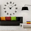 A modern living room with a large DIY wall clock, a black sofa with colorful cushions, and a white coffee table. Produktbild-Vorschau