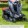A person is riding a lawnmower in a grassy yard. Produktbild-Vorschau
