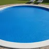 A round solar pool cover is shown floating on a pool of water, with a grassy area and lounge chairs in the background. Náhled obrázku produktu