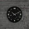 A round, black wall clock with a space-themed design, featuring glow-in-the-dark numbers and celestial illustrations, mounted on a gray brick wall. Náhled obrázku produktu