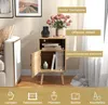 A wooden nightstand with an open shelf and a closed cabinet, decorated with flowers and a phone charger. Produktbild-Vorschau