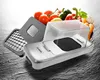 A kitchen gadget for chopping vegetables, with a pile of fresh vegetables in the background. Náhled obrázku produktu