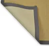 A close-up view of a rug corner, showing the textured surface and the dark gray border. The rug is partially lifted, revealing the underside. Voir les images du produit