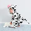 A baby wearing a cow costume is playing with a stuffed animal on a rug. Produktbild-Vorschau