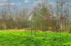 An empty metal frame for a pet enclosure is set up in a grassy field with trees in the background. Produktbild-Vorschau