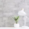 Light gray concrete block pattern peel and stick wallpaper on a wall behind a white desk lamp and a potted plant Produktbild-Vorschau