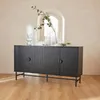 A dark gray sideboard with ribbed doors is placed on a wooden floor in front of a window with an arched opening. Several glass vases and a branch with leaves are placed on top of the sideboard. Produktbild-Vorschau