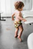 A toddler is standing and reaching for a chair. Produktbild-Vorschau