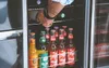 A person's hand is reaching into a refrigerator stocked with bottles of drinks. Produktbild-Vorschau
