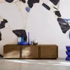 A wooden TV cabinet with three doors is placed against a wall with a large, abstract, multi-colored pattern. Decorative items are placed on top of the cabinet. Anteprima dell’immagine prodotto
