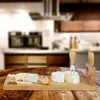 A cheese board with cheese and knives on a wooden table, with a blurred kitchen background. Náhľad obrázku produktu