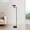 A black projector stand is shown in a room with a couch and a window with a view of trees and mountains. Podgląd zdjęcia produktu