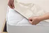 Hands are shown adjusting a cream-colored fitted sheet over a white mattress. Produktbild-Vorschau
