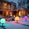 A snowy garden at dusk, decorated with colorful solar globe lights and string lights on a house and trees. Anteprima dell’immagine prodotto