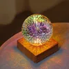 A decorative LED lamp with a glass sphere displaying a colorful, starburst-like pattern, placed on a wooden base. Produktbild-Vorschau