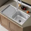 A stainless steel kitchen sink with a draining board, faucet, and some fruit on the countertop. Produktbild-Vorschau