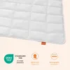 A close-up of a white quilted blanket with several certification icons and text below. Produktbild-Vorschau