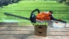A Stihl hedge trimmer is displayed on a wooden surface with a green grassy background. A cardboard box with hazard symbols is placed in front of the hedge trimmer. Produktbild-Vorschau
