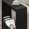 A black side table next to a sofa, with books and a cup of tea on it. Produktbild-Vorschau