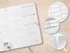 An open planner with detailed close-ups of its pages and calendar views, set against a wooden background. Voir les images du produit