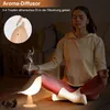 A woman meditating in a dimly lit room with a bird-shaped aroma diffuser lamp emitting smoke. Produktbild-Vorschau