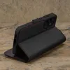 A black leather phone case with red stitching is displayed on a textured surface. Anteprima dell’immagine prodotto