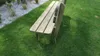 A wooden garden bench sits on a lush green lawn next to a path of white gravel and some plants. Produktbild-Vorschau