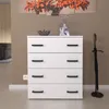 A white chest of drawers with black handles is shown in a room with a brown wall and a painting of autumn leaves above it. An umbrella stand with an umbrella is to the right. Produktbild-Vorschau