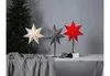 Three star-shaped lamps are displayed on a table next to a Christmas tree. Podgląd zdjęcia produktu