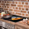 A glass cutting board with a fire and water design is placed on a kitchen counter in front of a brick backsplash. A frying pan is on the cutting board, and vegetables are on a wooden cutting board to the right. Produktbild-Vorschau