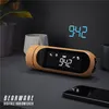 A digital alarm clock with a wooden finish is placed on a dark surface next to a smartphone and some decorative pots. Produktbild-Vorschau