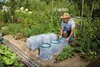 A man is tending to plants in a garden, placing protective covers over them. Voir les images du produit