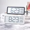 Two digital clocks are shown, one black and one white, placed on top of books. Produktbild-Vorschau