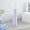 A white electric water flosser sits on a light gray countertop next to a vase of flowers and folded blue towels. Produktbild-Vorschau