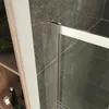 Close-up view of a shower door frame against a tiled wall and a shelf with bathroom items. Produktbild-Vorschau