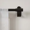 A close-up view of a black curtain rod mounted on a white wall, with a white linen curtain partially visible. Podgląd zdjęcia produktu